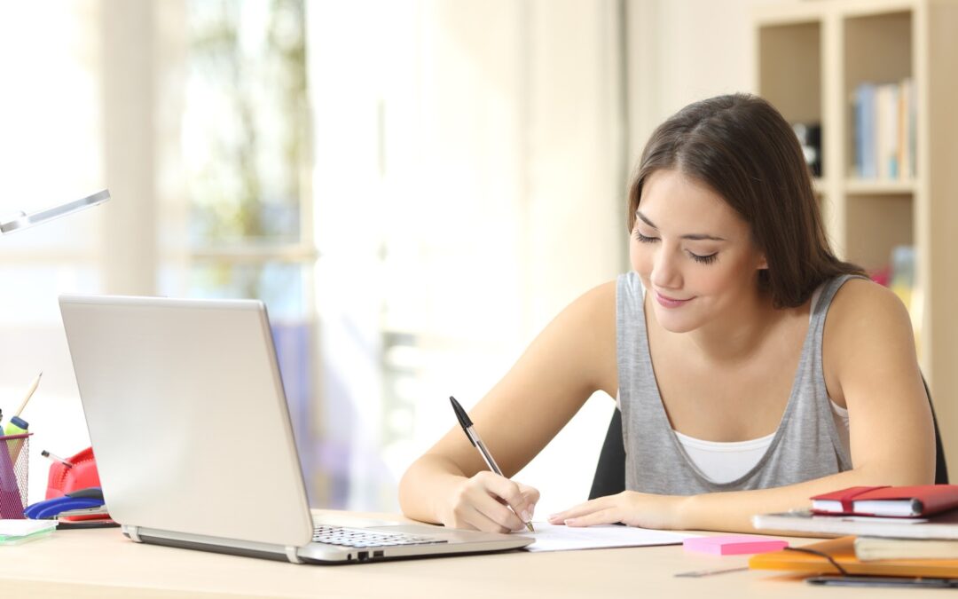 Beautiful student studying on line and learning writing notes in a desk at home